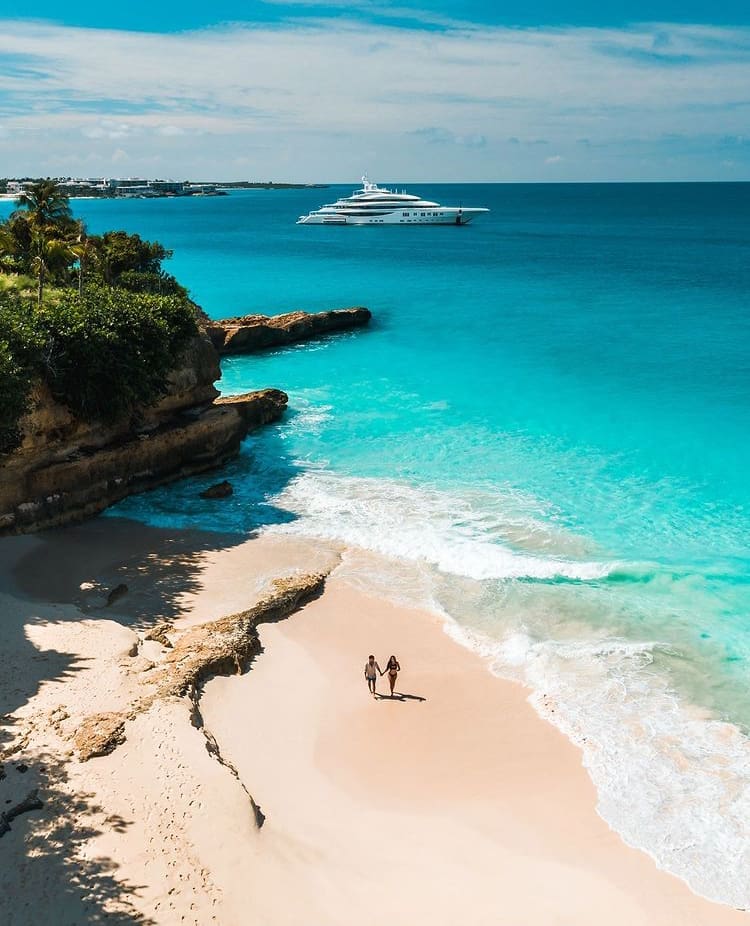 A couple walk hand in hand along a private beach in Anguilla
