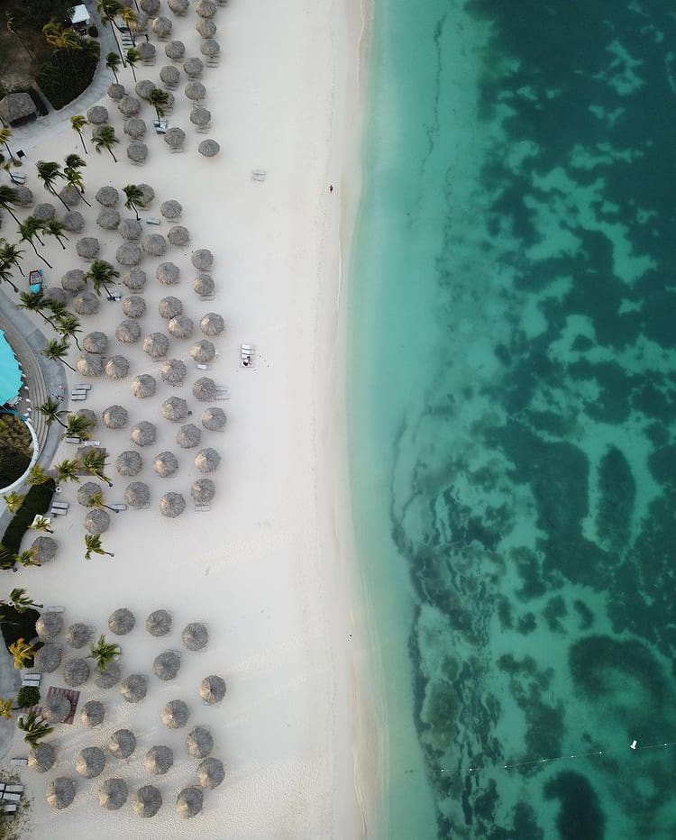 White sand, beach umbrellas and blue sea in Aruba - The 15 Best Islands In The Caribbean