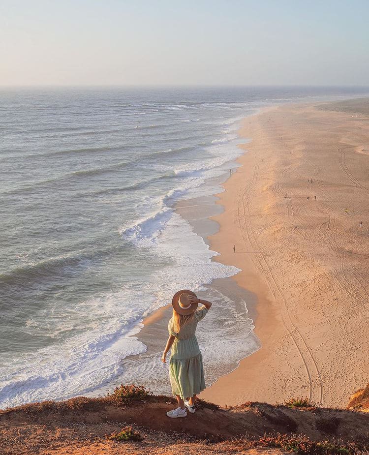 A woman watches the wave break at Praia do Nazare - The 10 Most Beautiful Beaches In Portugal
