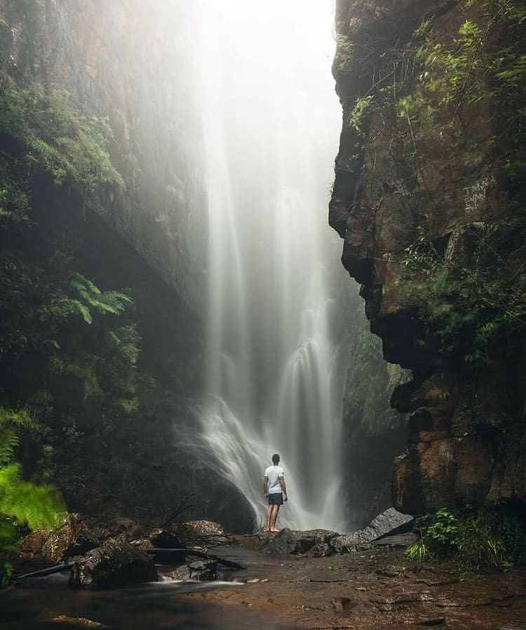 A young man standing at the base of a waterfall - Is It Safe to Visit South Africa In 2022?