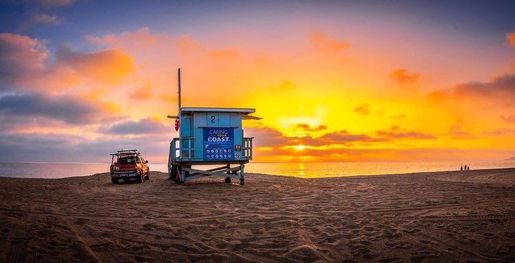 The sun sets over a lifeguard hut and vehicle at zuma beach, Malibu