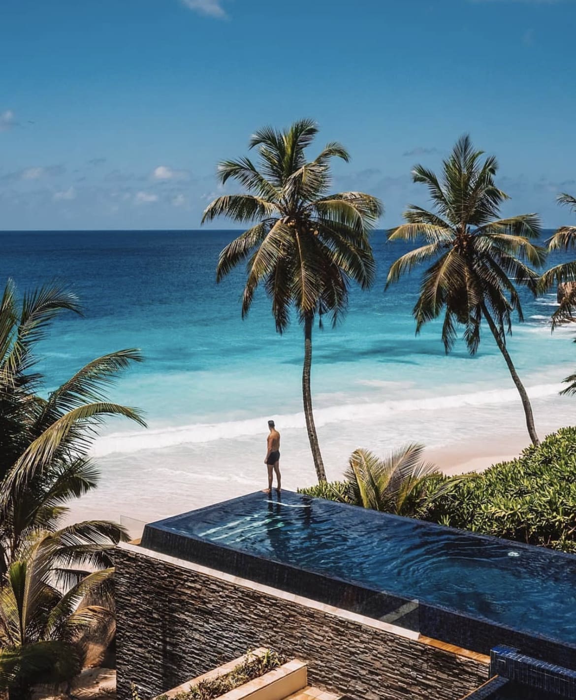 A young man stands at the edge of an infinity pool at a resort in the Seychelles